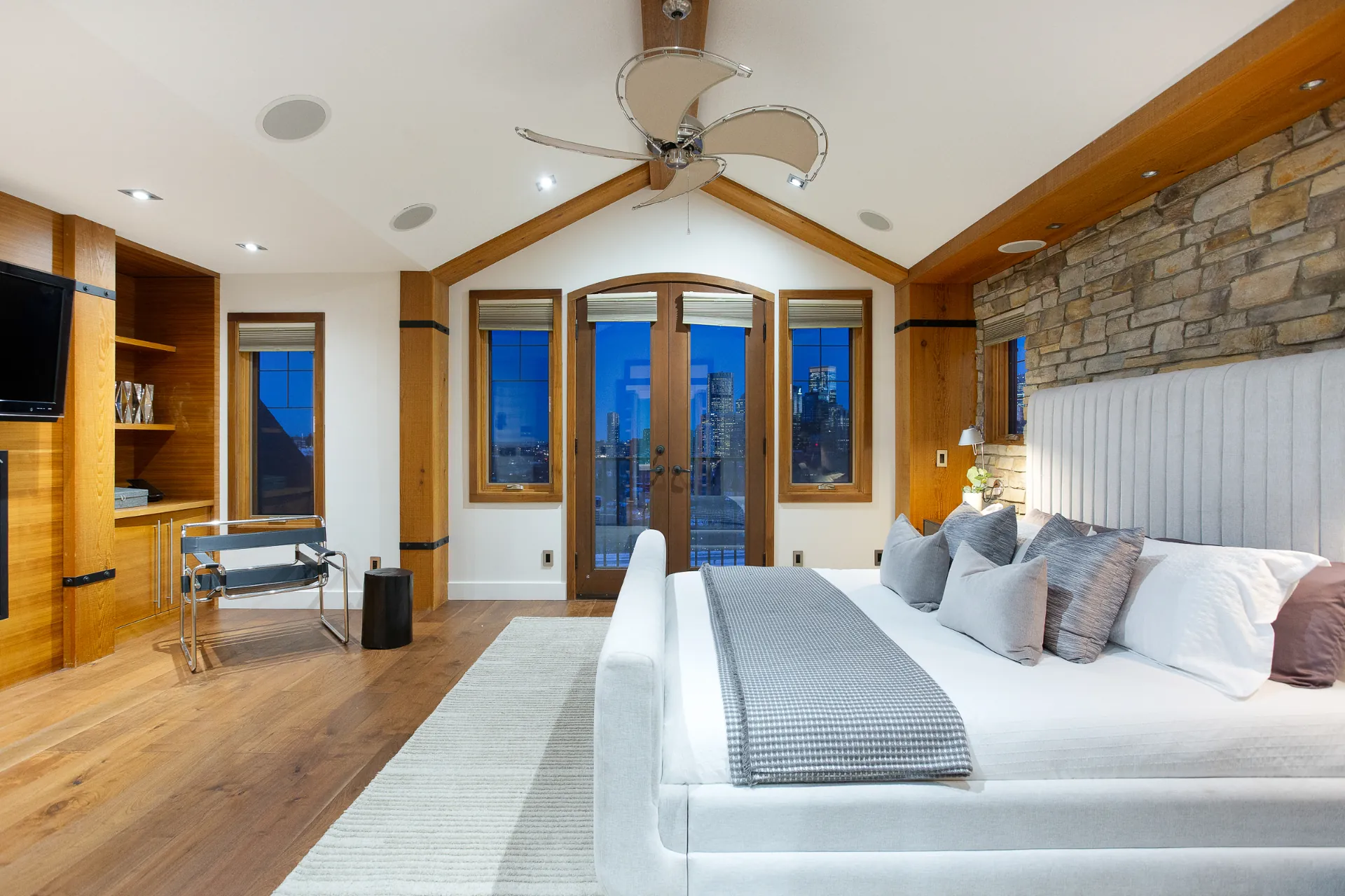 Primary bedroom with vaulted ceiling, stone wall and French doors to the skyline